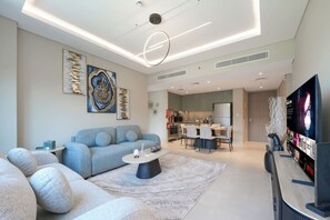 A modern living room with a sofa, coffee table, and a TV. There is a kitchen area with a dining table and chairs. - Elegant 2BR Haven in Viridian by Central Park (Dubai)