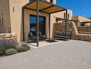 A modern outdoor patio with a pergola, stone walls, and outdoor furniture. - Elafonisos Village Boutique Residences (Elafonisos)