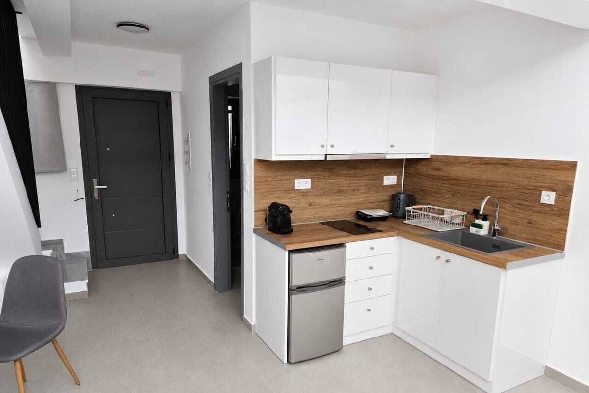 Eine kompakte Küche mit weißen Schränken, einem Edelstahlkühlschrank, einer Holz Arbeitsplatte und einem Spülbecken.