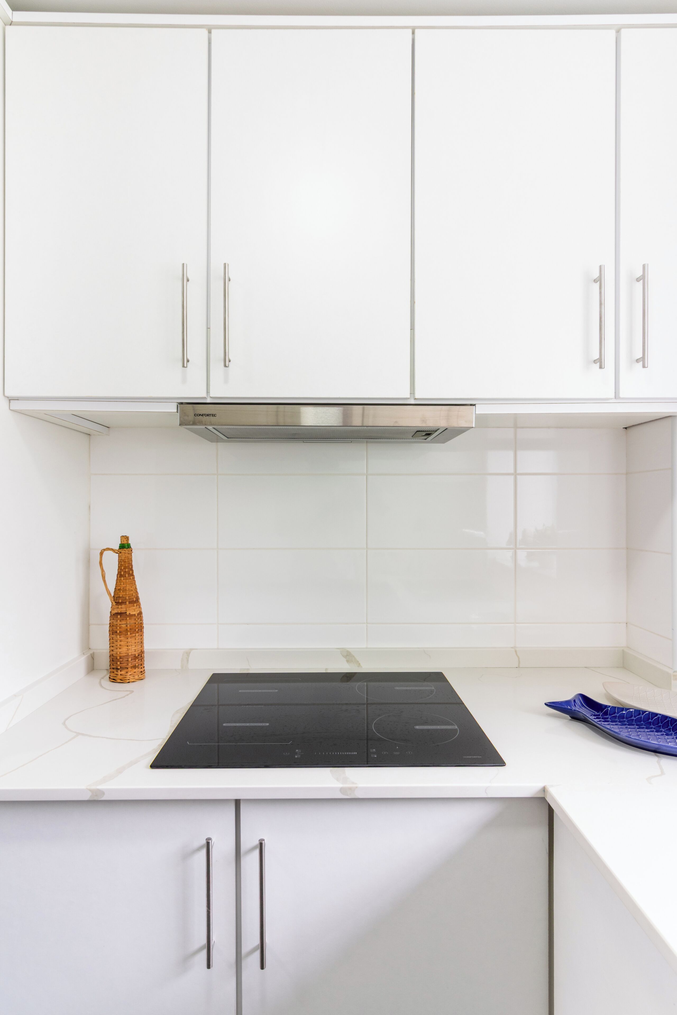 Een moderne keuken met witte kastjes, een roestvrijstalen afzuigkap en een zwart inductiekookplaat.