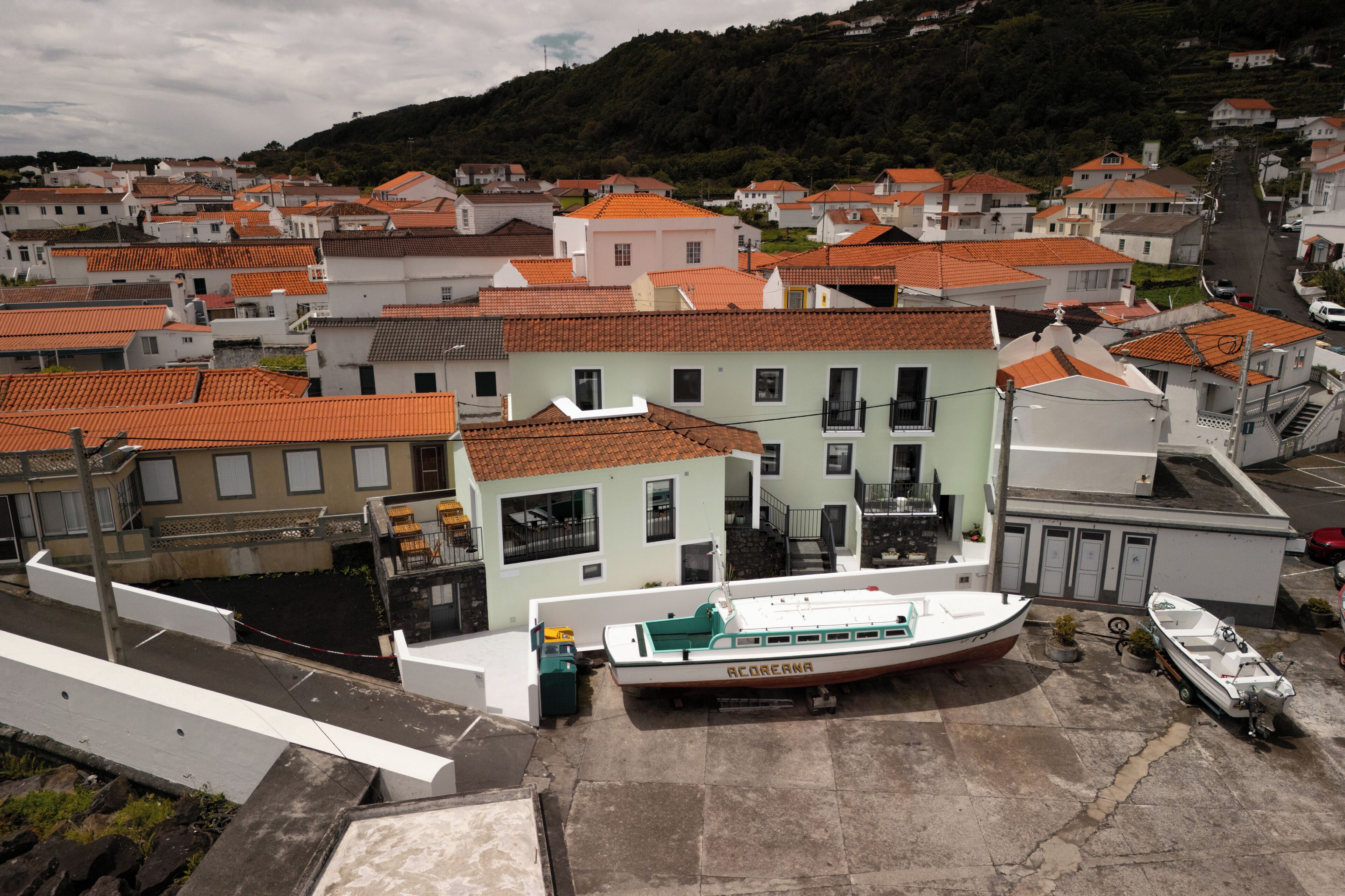 A coastal town with terracotta-roofed buildings, a marina with boats, and a hillside in the background.