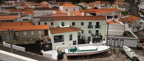 A coastal town with terracotta-roofed buildings, a marina with boats, and a hillside in the background.
