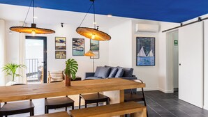 Een modern interieur met een houten eettafel, banken, een bank en hangende rieten lampen.