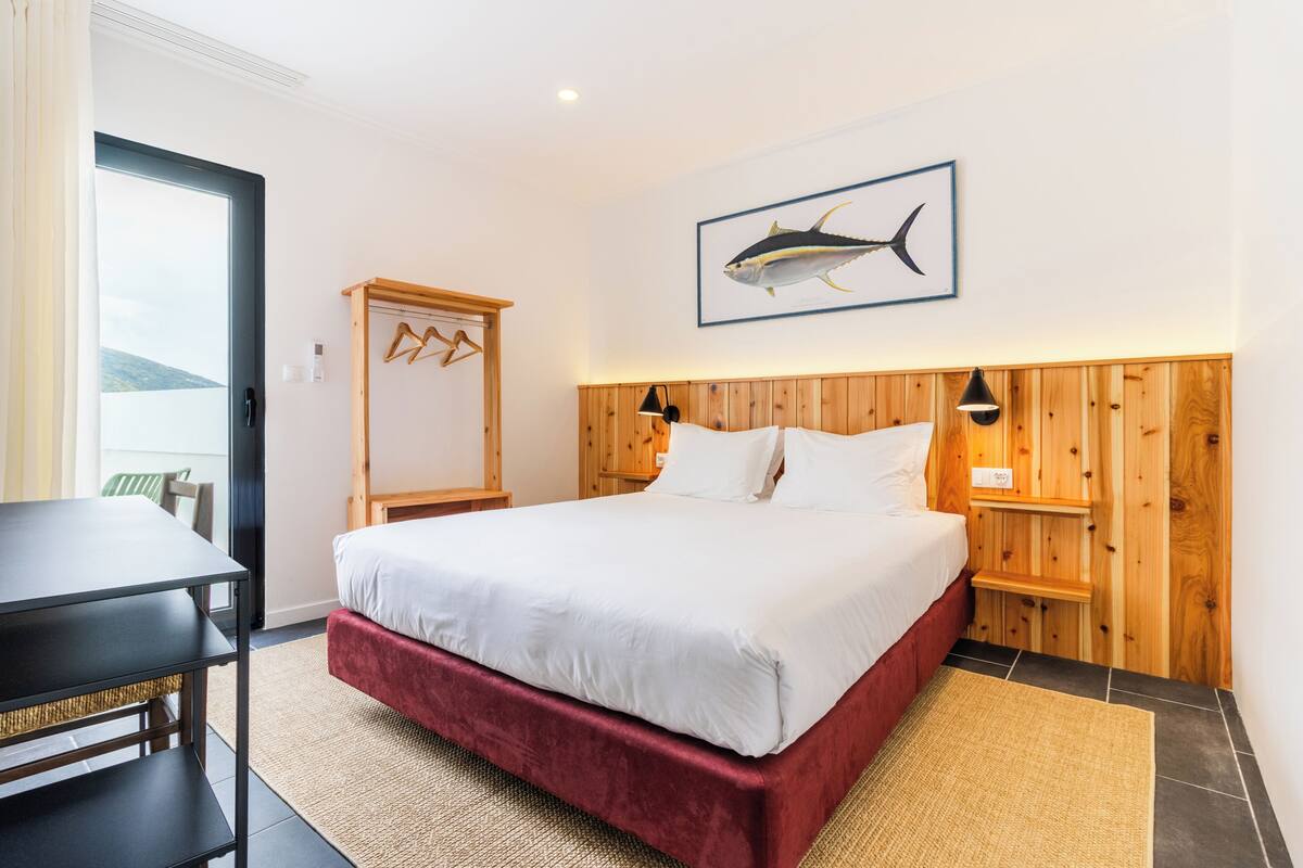 Habitación de hotel con cama, escritorio, armario de madera, un cuadro de peces enmarco y vistas al exterior.