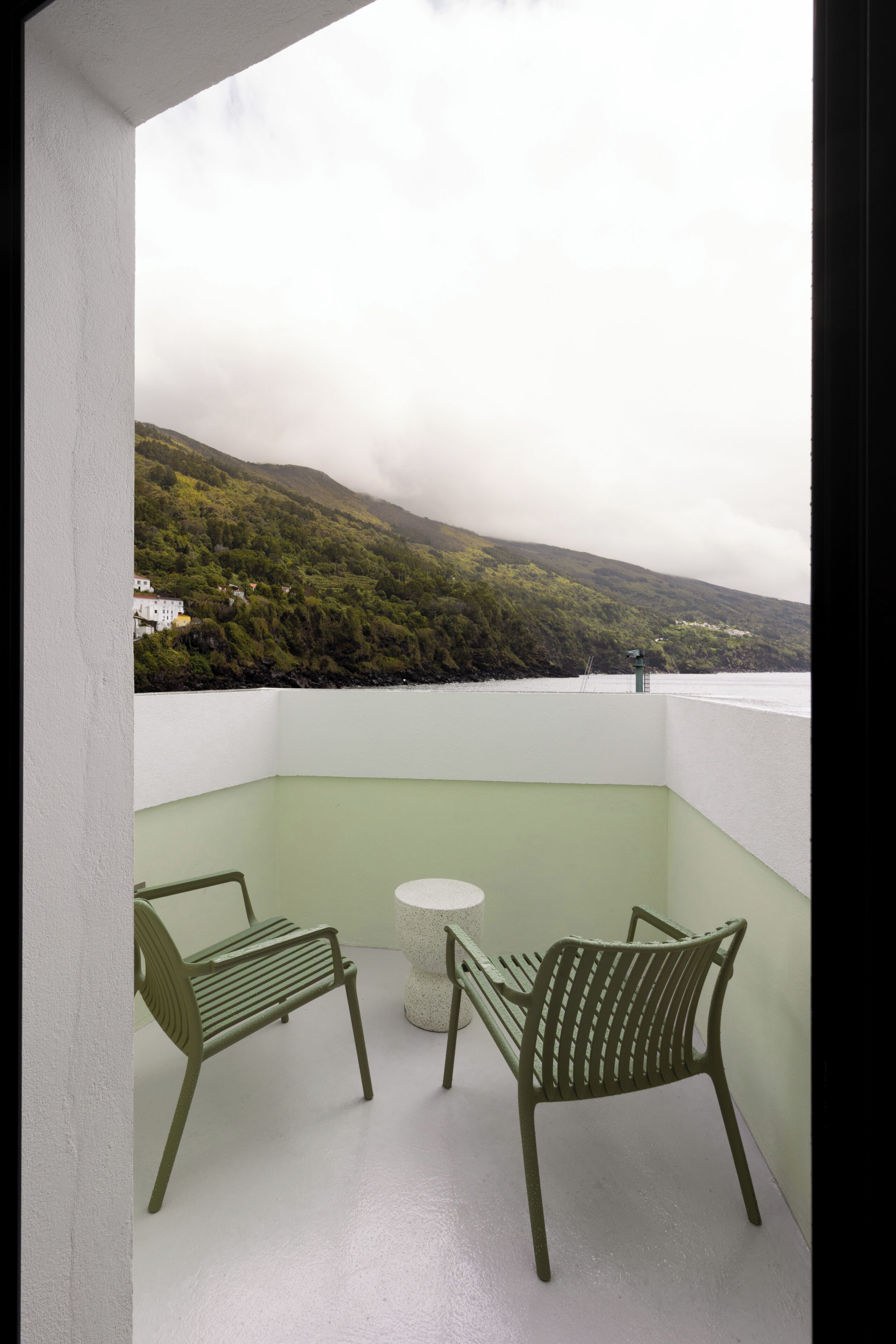 A balcony with two chairs and a small table, overlooking a mountainous landscape.