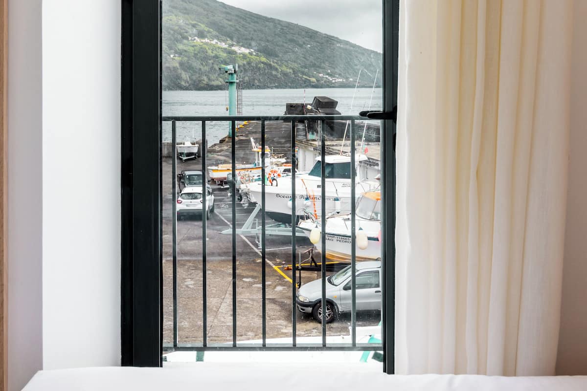 Una habitación con una cama, un ventanal con vista al puerto y una cortina.