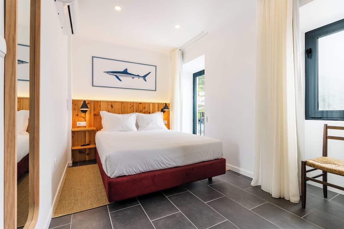 Un dormitorio con una cama, cabecero de madera, lámparas de noche, una alfombra, una silla y un cuadro en la pared.