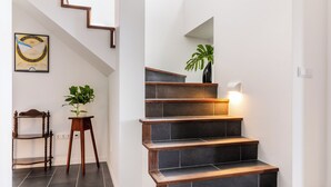 Een trap met donkere tegels, een houten leuning en een plant in een pot op de overloop.