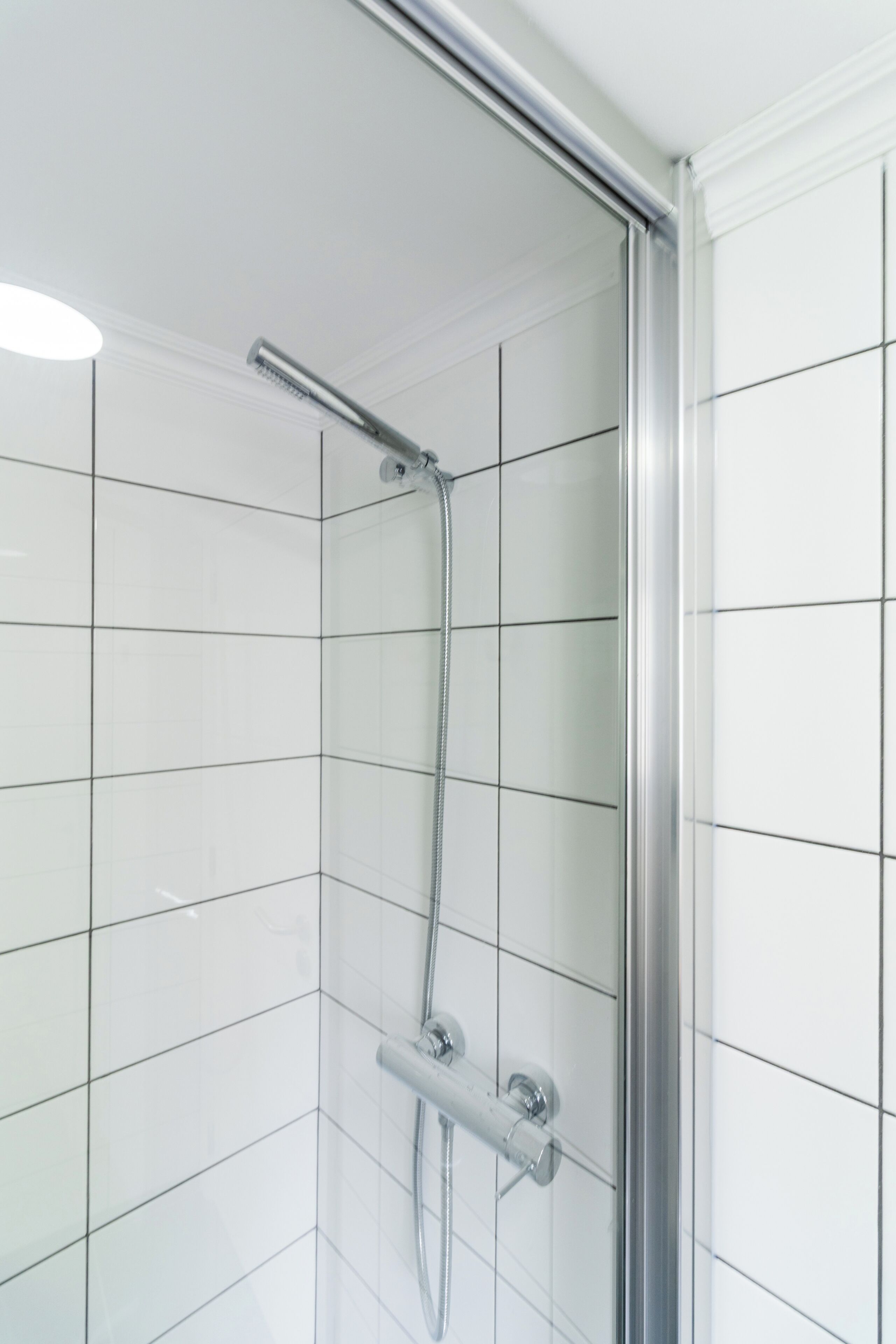 Ducha con puerta de vidrio, accesorios cromados y paredes de azulejos blancos.