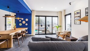 Een moderne woonkamer met een houten eettafel, grijze banken en uitzicht op een zwembad door grote ramen.