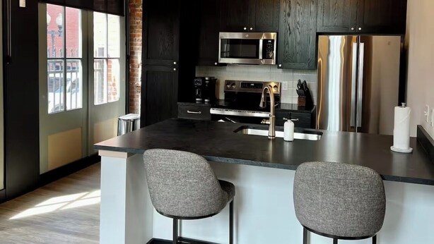 A modern kitchen with a central island, bar stools, stainless steel appliances, and a wooden ceiling. - Brick & Bed - Walk to Arch/Stadium - Downtown Loft (St. Louis)