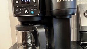 A Keurig coffee maker with a digital display, a carafe, and a pod holder on a kitchen counter. - Brick & Bed - Walk to Arch/Stadium - Downtown Loft (St. Louis)