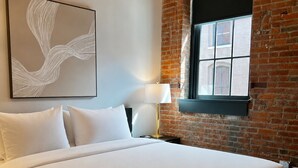 A bed in a room with a brick wall, a window, and a wall-mounted artwork. - Brick & Bed - Walk to Arch/Stadium - Downtown Loft (St. Louis)