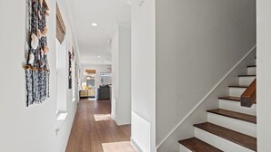 Ein modernes Interieur mit einer Holztreppe, einem Flur mit einer hängenden Muscheldekoration und einem Blick in einen Küchenbereich.