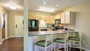 A modern kitchen with wooden cabinets, a granite countertop, and a built-in island with bar stools. - Eagle Trace Two Bedroom Condo (Mc Gaheysville)
