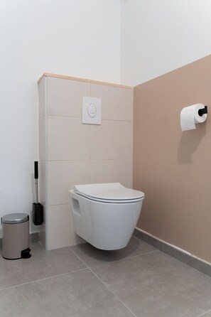 Ein modernes Badezimmer mit Toilette, Mülleimer und Toilettenpapierhalter an der Wand.