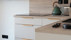 A modern kitchen with a flat-screen TV mounted on the wall, wooden cabinets, a countertop, and a kettle. - Studio Calypso 20 m from the sea (Mauguio)