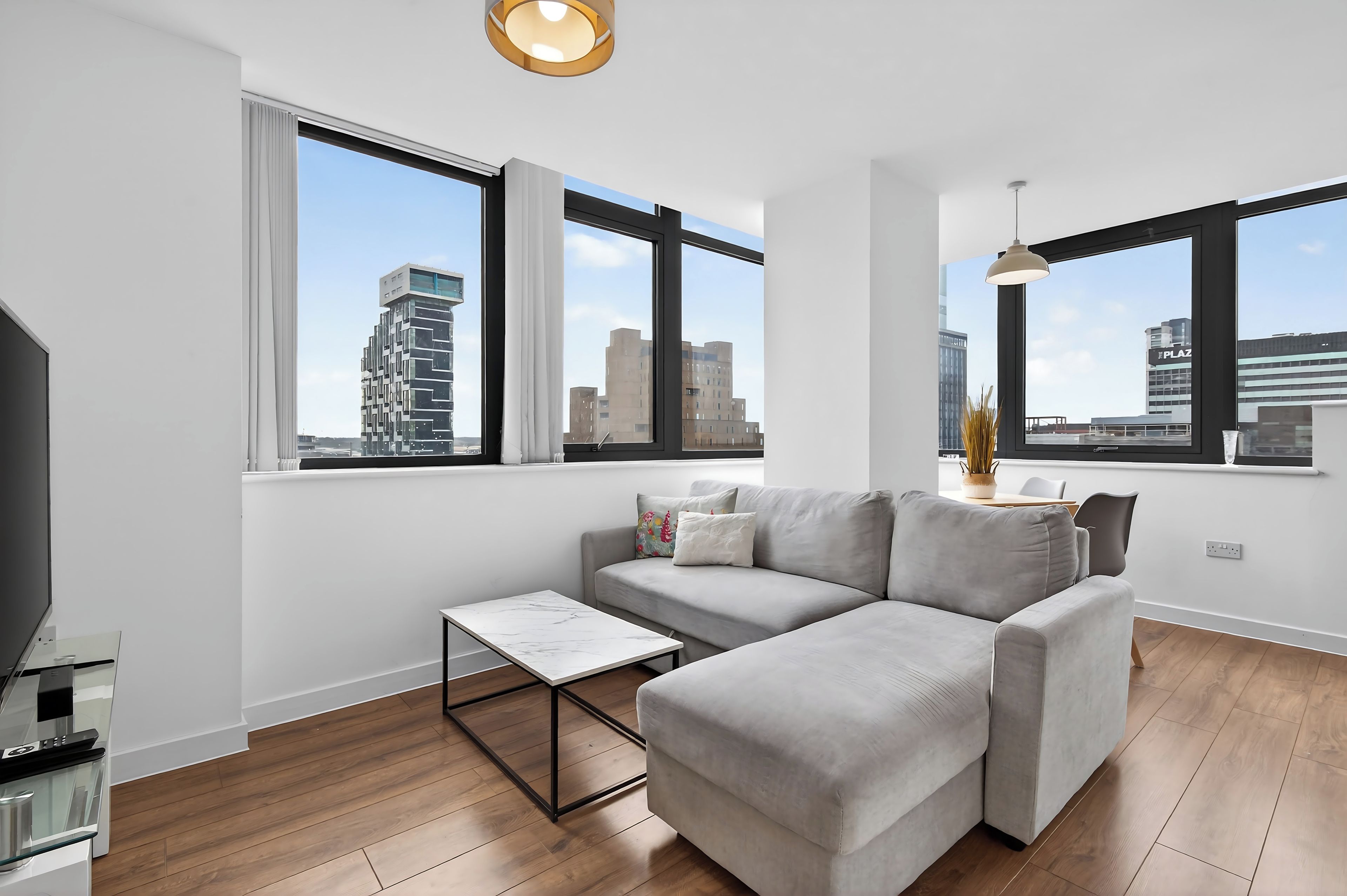 A modern living room with a sectional sofa, a small coffee table, and large windows offering city views.