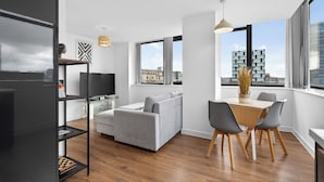 En moderne stue med en grå sofa, et spisebord med stole, og et stort vindue med udsigt over byen.
