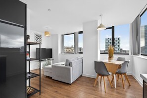 Ein modernes Wohnzimmer mit einem grauen Sofa, einem Esstisch mit Stühlen und einem großen Fenster mit Blick auf die Stadt.