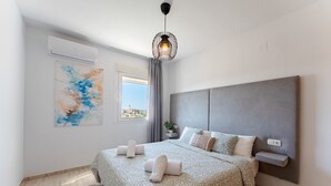 Un dormitorio moderno con una cama grande, cabecera gris, aire acondicionado de pared, una lámpara colgante original y ventana con vistas.