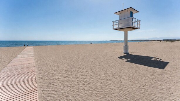 Ein Rettungsschwimmturm am Strand, verbunden durch eine Holzpromenade.