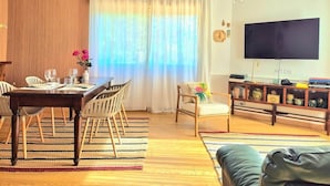 Ein Wohnzimmer mit Esstisch, Stühlen, einer Couch, einem Fernseher und einem Holzkabinett.