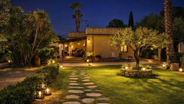 Ein gut beleuchteter Außenbereich mit einem gepflasterten Weg, der zu einem Gebäude führt, umgeben von Grünflächen und Palmen.