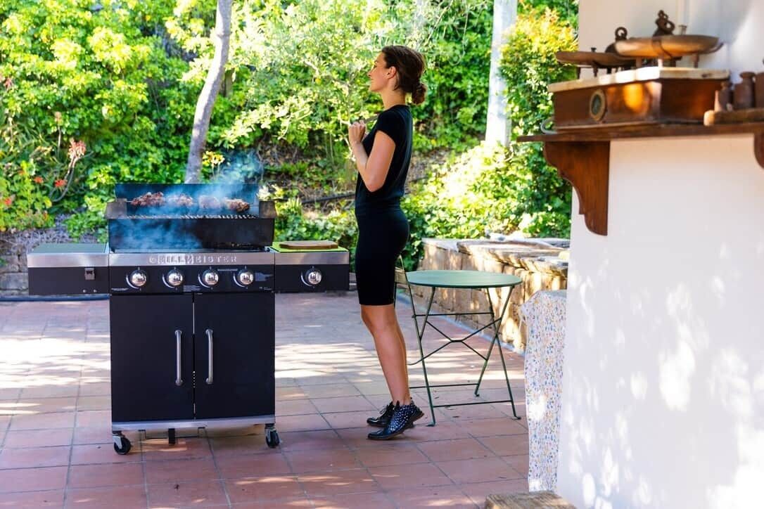 A person standing by a portable grill with a view of greenery in the background.