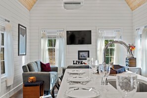 A modern interior with a dining area, a sofa, a TV, and a kitchen counter. - Shenandoah, Firepit, peaceful Cabin w/salt water Hot tub! (Luray)