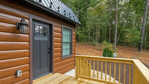 Una baita di legno con una porta d'ingresso, una finestra, un patio e un tetto in metallo.