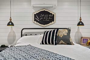 Una cama bien hecha con una colcha estampada, un cojín decorativo y un letrero en la pared con una cita.
