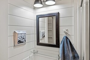 A bathroom with white paneled walls, a dark-framed mirror, a towel rack with a towel, and a framed picture on the wall. - Shenandoah, Firepit, peaceful Cabin w/salt water Hot tub! (Luray)