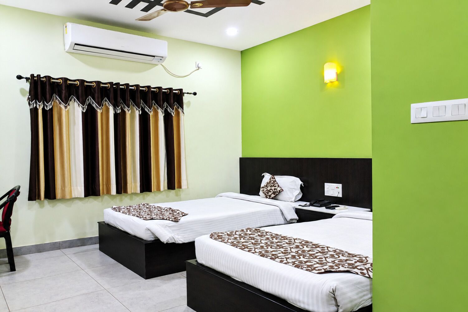 A hotel room with two beds, a ceiling fan, an air conditioning unit, and a green accent wall.