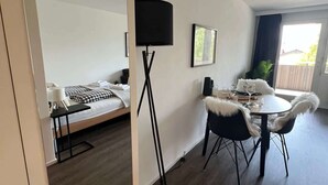 A modern room with a bed, a dining table with chairs, a floor lamp, and a large mirror. - book2stay: Retro-Alpin Studio with balcony (Laax)
