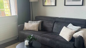 A living room with a dark grey sofa, a round black coffee table, and a small potted plant. There are two framed pictures on the wall. - book2stay: Retro-Alpin Studio with balcony (Laax)