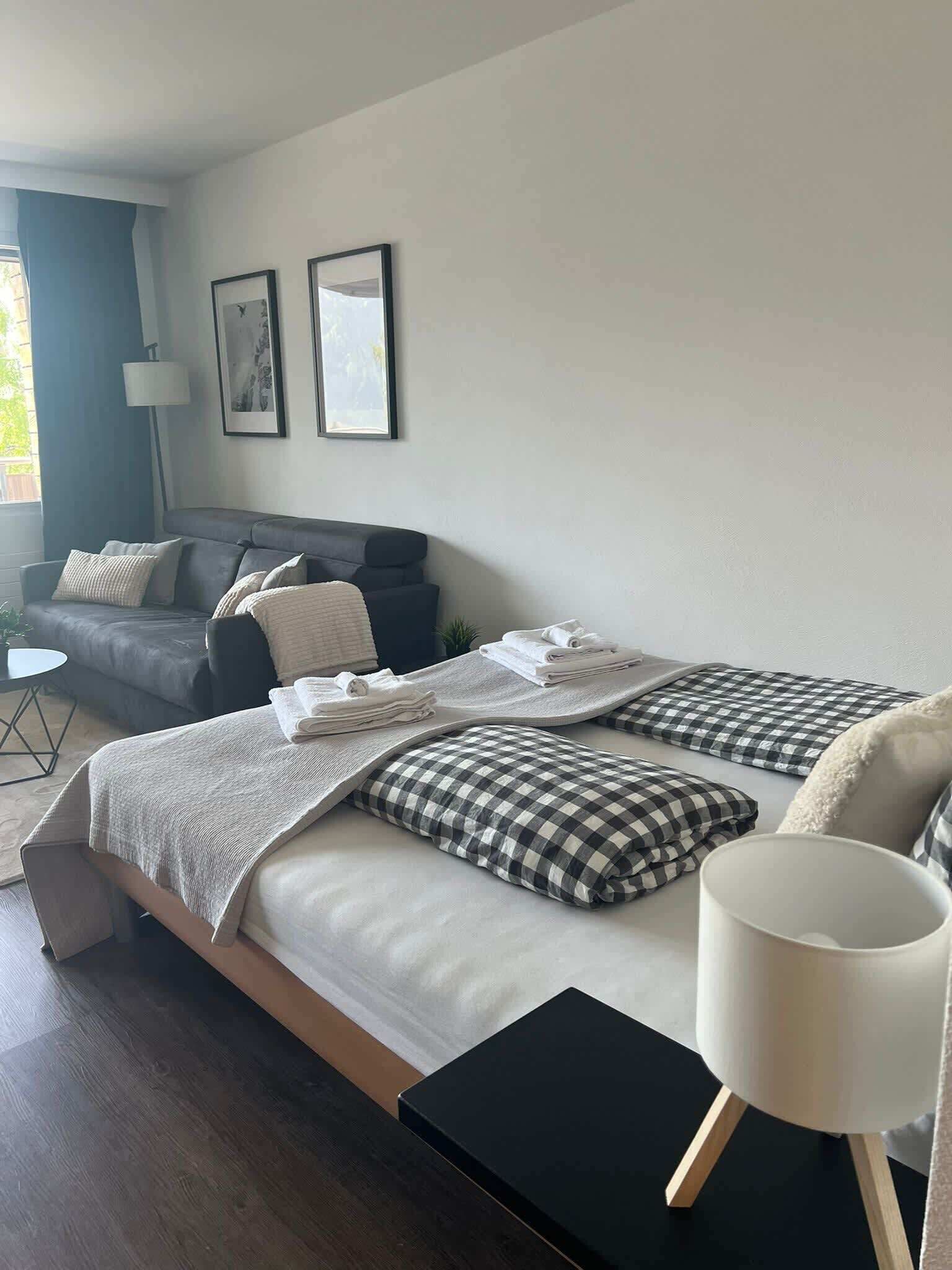 A modern bedroom with a bed, a side table, a lamp, a sofa, and a framed picture on the wall.