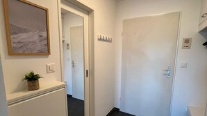 A hallway with a door, a framed picture, a small plant, and a light fixture. - book2stay: Retro-Alpin Studio with balcony (Laax)