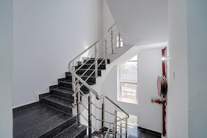 Una escalera con barandillas de metal y peldaños negros, que conduce a una puerta con pomo rojo.