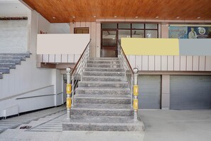 Un escalier avec des marches en marbre et des rampes en métal, menant à une entrée dotée de portes en verre et d’une enseigne.