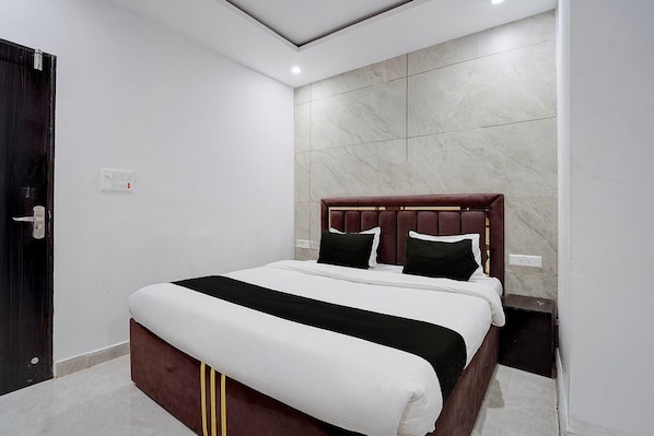 A neatly made bed with a wooden headboard, a bedside table, and a wall-mounted power outlet.