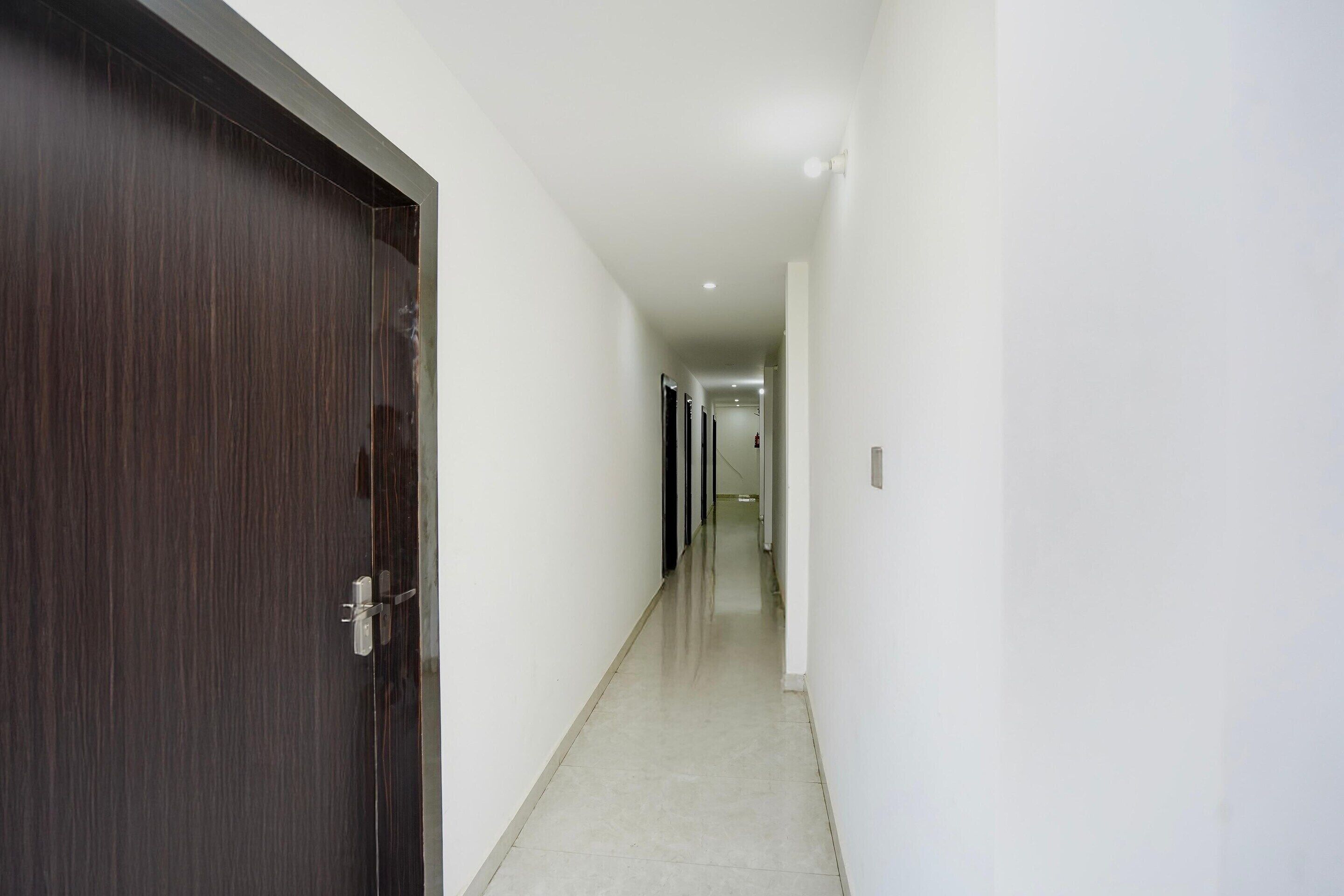 A corridor with a dark wooden door on the left, white walls, and a tiled floor.