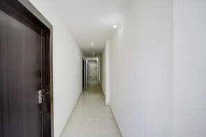 Un couloir avec une porte en bois sombre sur la gauche, des murs blancs et un sol carrelé.