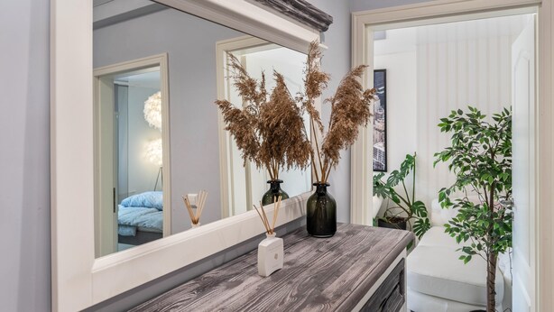 A bathroom with a mirror, two vases with dried plants, a small white device on the counter, and a potted plant.