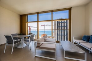 A modern living room with a dining table, chairs, a sofa, and a large window with a view of the ocean and buildings. - Intempo by Holuxe - 074 - 7th floor (Benidorm)
