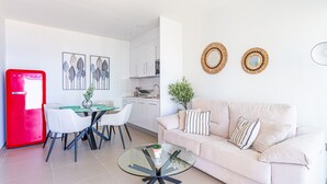 A modern kitchen with white cabinets, a dining area with a glass table, and a living room with a beige sofa. - Intempo by Holuxe - 075 - 7th floor (Benidorm)