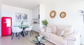 A modern kitchen with white cabinets, a dining area with a glass table, and a living room with a beige sofa. - Intempo by Holuxe - 075 - 7th floor (Benidorm)