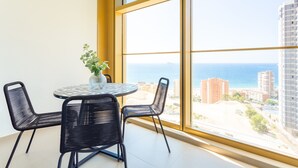 A room with a large window, a round table with chairs, and a vase with flowers. - Intempo by Holuxe - 075 - 7th floor (Benidorm)