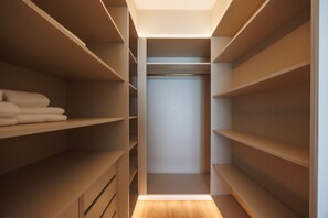 Ein begehbarer Kleiderschrank mit mehreren Regalen und einer Kleiderstange, mit Holzboden und einer beleuchteten Decke.