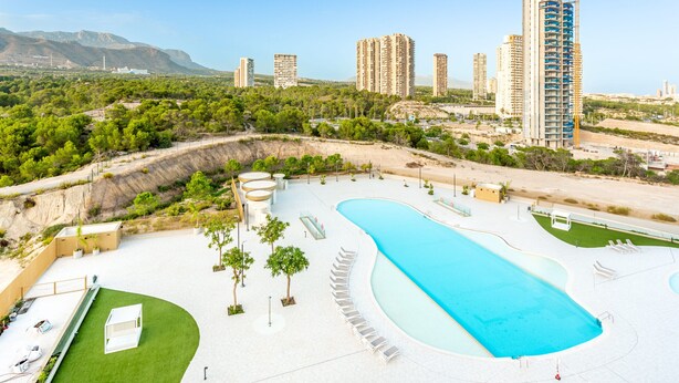Ein Resort mit einem großen Schwimmbad, mehreren Hochhäusern und einer Bergkulisse.